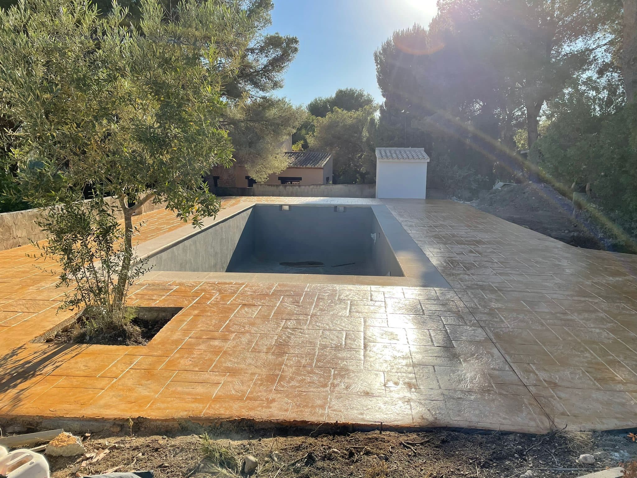 Vista general del pavimento de hormigón impreso con los dos acabados, junto a la piscina y el olivo