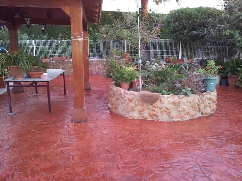 Porche con pavimento de hormigón impreso en rojo, con jardinera de piedra y plantas