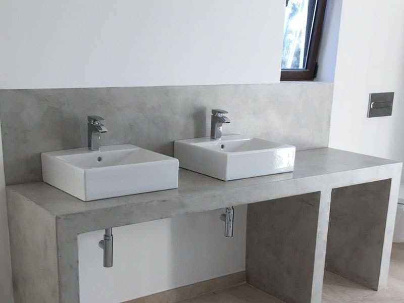 Baño revestido en microcemento gris claro con encimera continua y dos lavabos