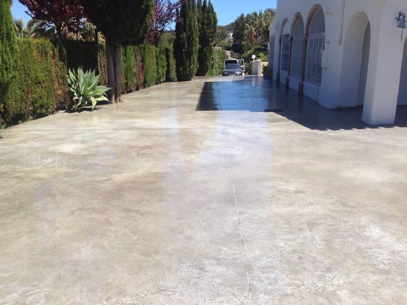 Acceso en hormigón pulido color crema entre cipreses, en una vivienda de urbanización