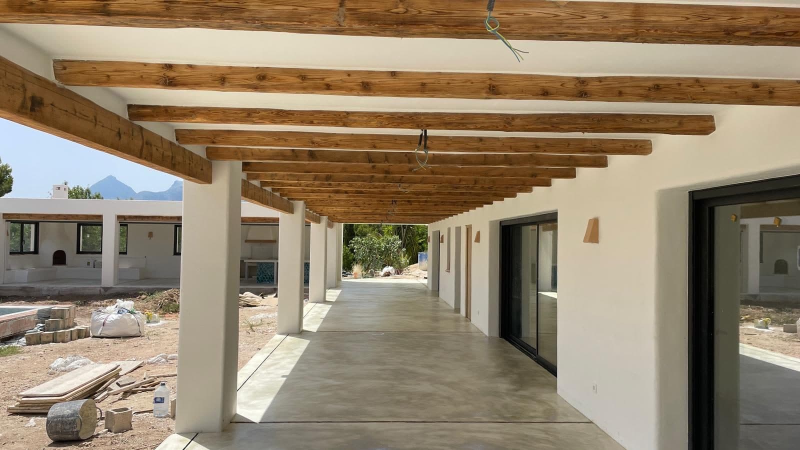 Porche de vivienda con vigas de madera y suelo de hormigón fratasado fino